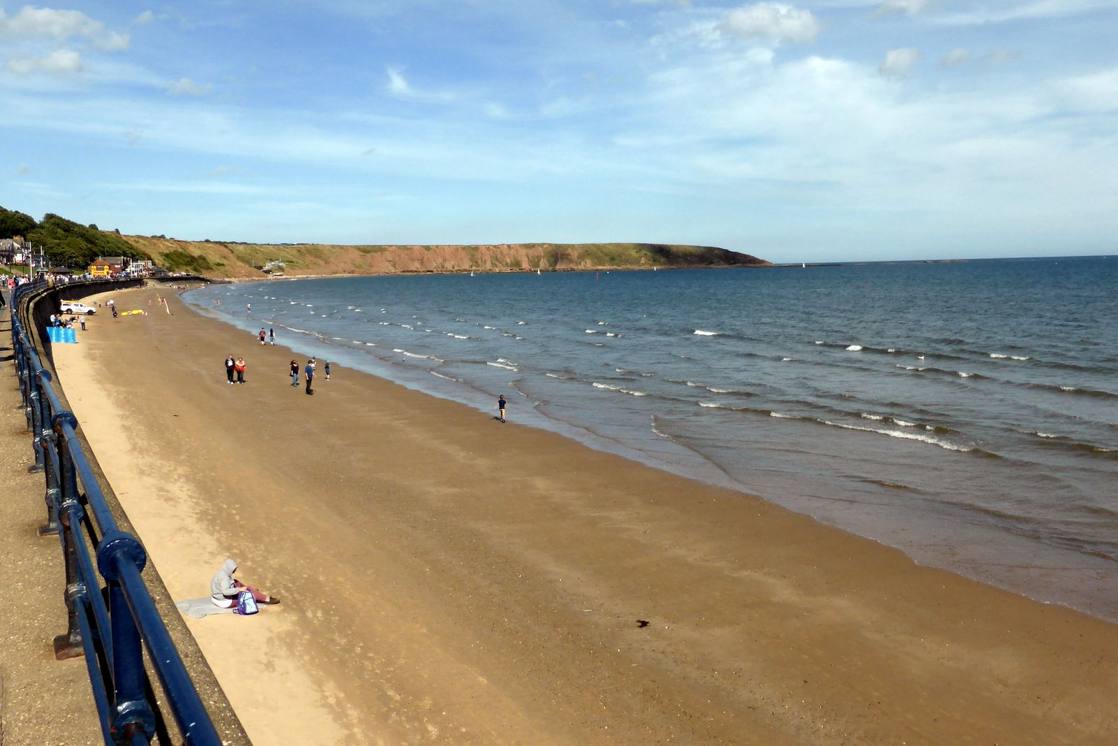 Filey Bay on a sunny day: the golden sands curving round to the green headland of Carr Naze, seen from the promenade railings